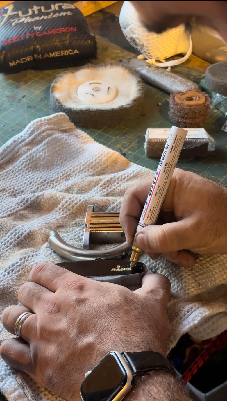 Applying paint to the lettering on a golf club head during refurbishment.